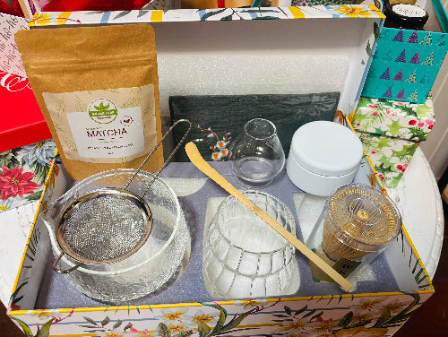 Tea-making set with matcha powder, strainer, and other accessories in a decorative box.